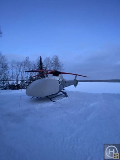 Helicopter covered in a protective cover, parked in the snow.