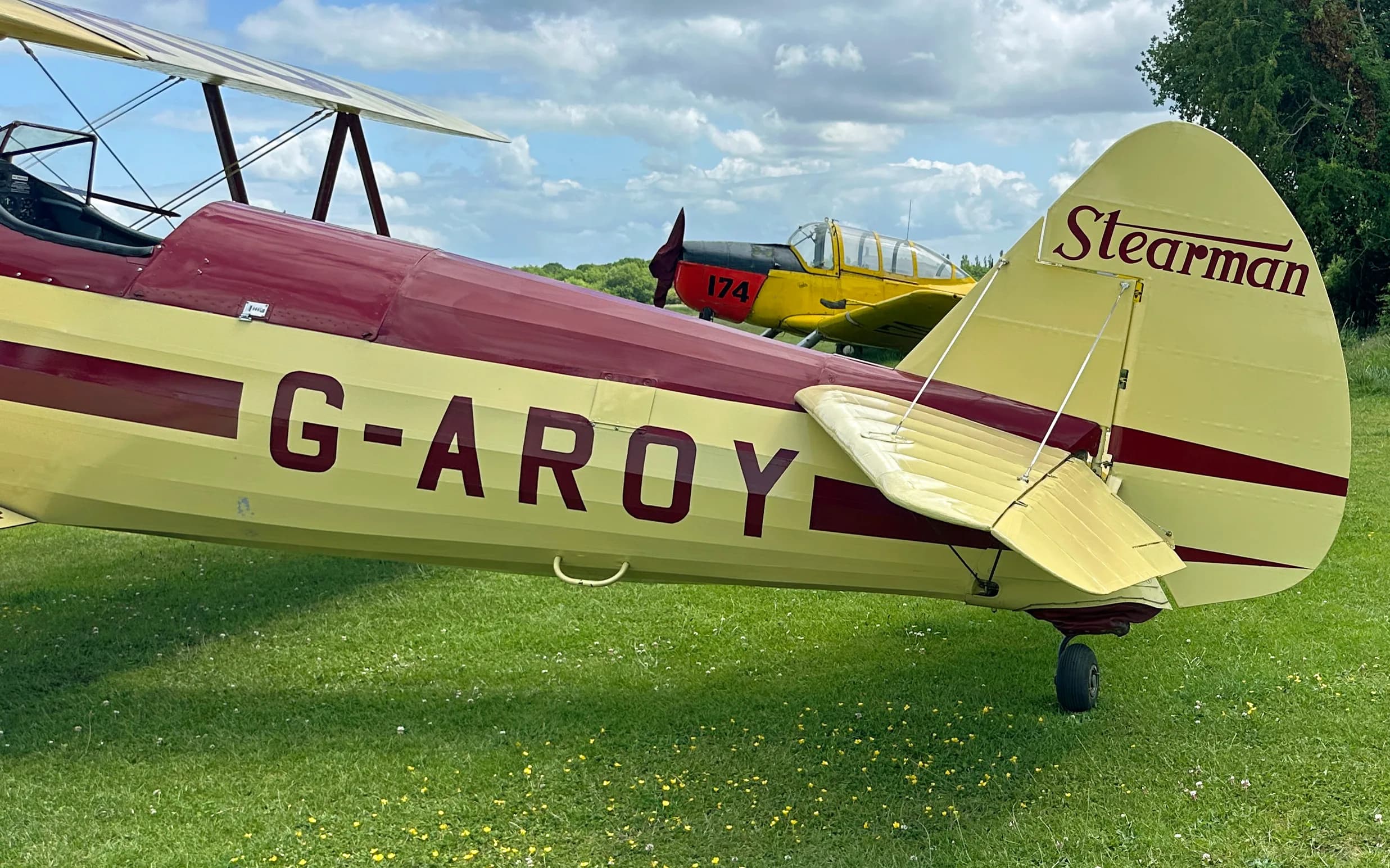 The tail section of the yellow and red Stearman biplane, G-AROY, with another yellow biplane in the background.