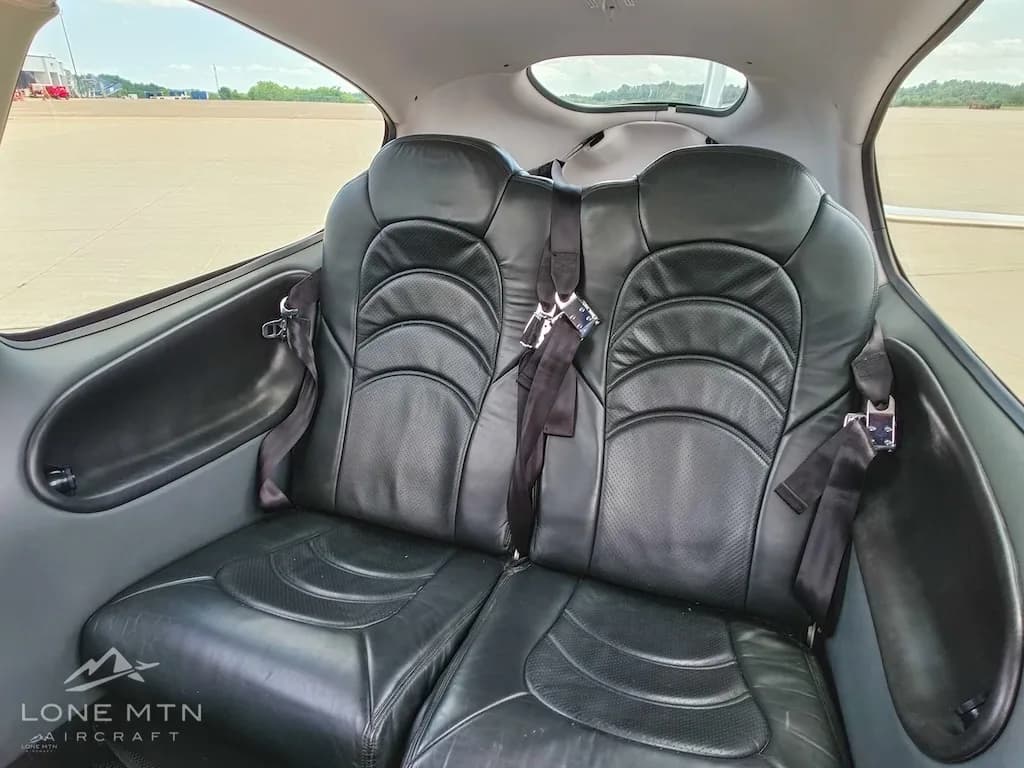 The black leather rear passenger seats of a Cirrus SR22 aircraft cabin, with seatbelts fastened.