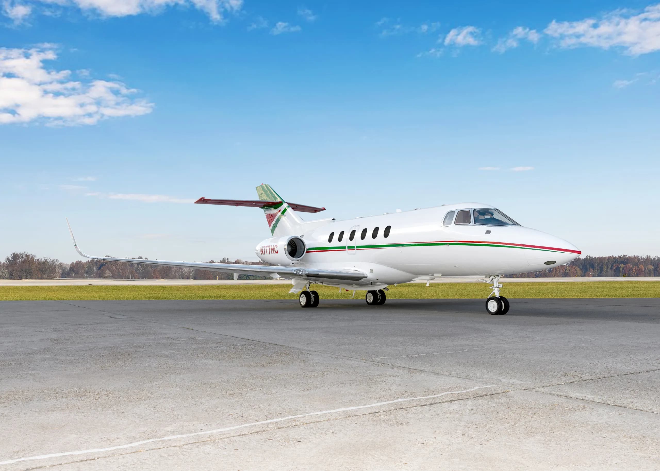 A white business jet with green and red stripes on the fuselage and tail, parked on an airfield from a front-side view.