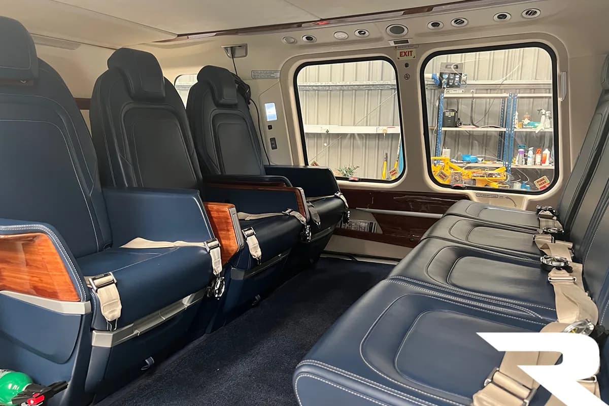 Interior view of a helicopter cabin with blue leather seats and wood trim, looking towards the rear.