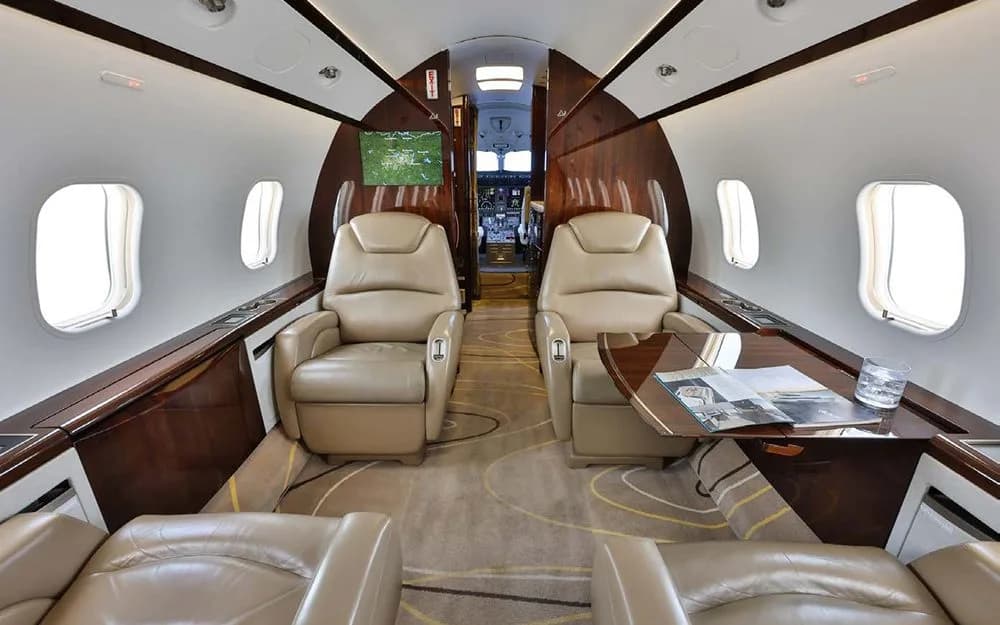 The luxurious interior cabin features tan leather seats, wood paneling, and a view towards the cockpit.