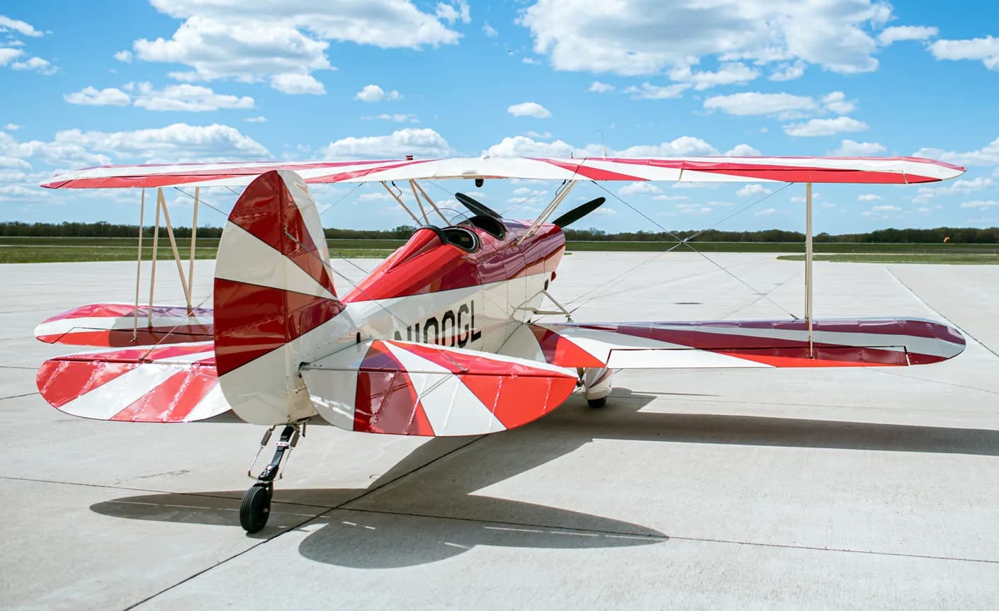 Rear view of a red and white biplane with tail number N100GL on the tarmac.