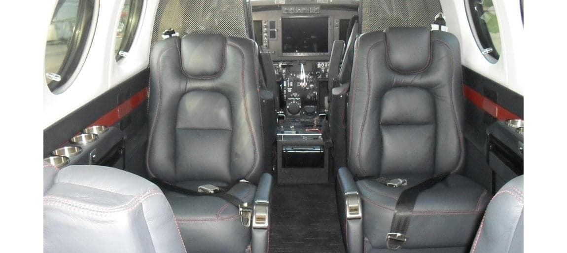 The interior of the Beechcraft King Air 350 features black leather seats with red stitching and a view towards the cockpit.
