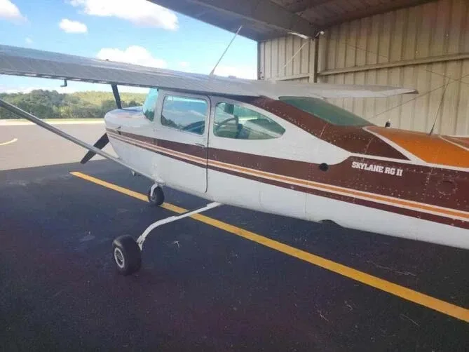 A side view of a white and brown Cessna Skylane RG II aircraft parked under a hangar.