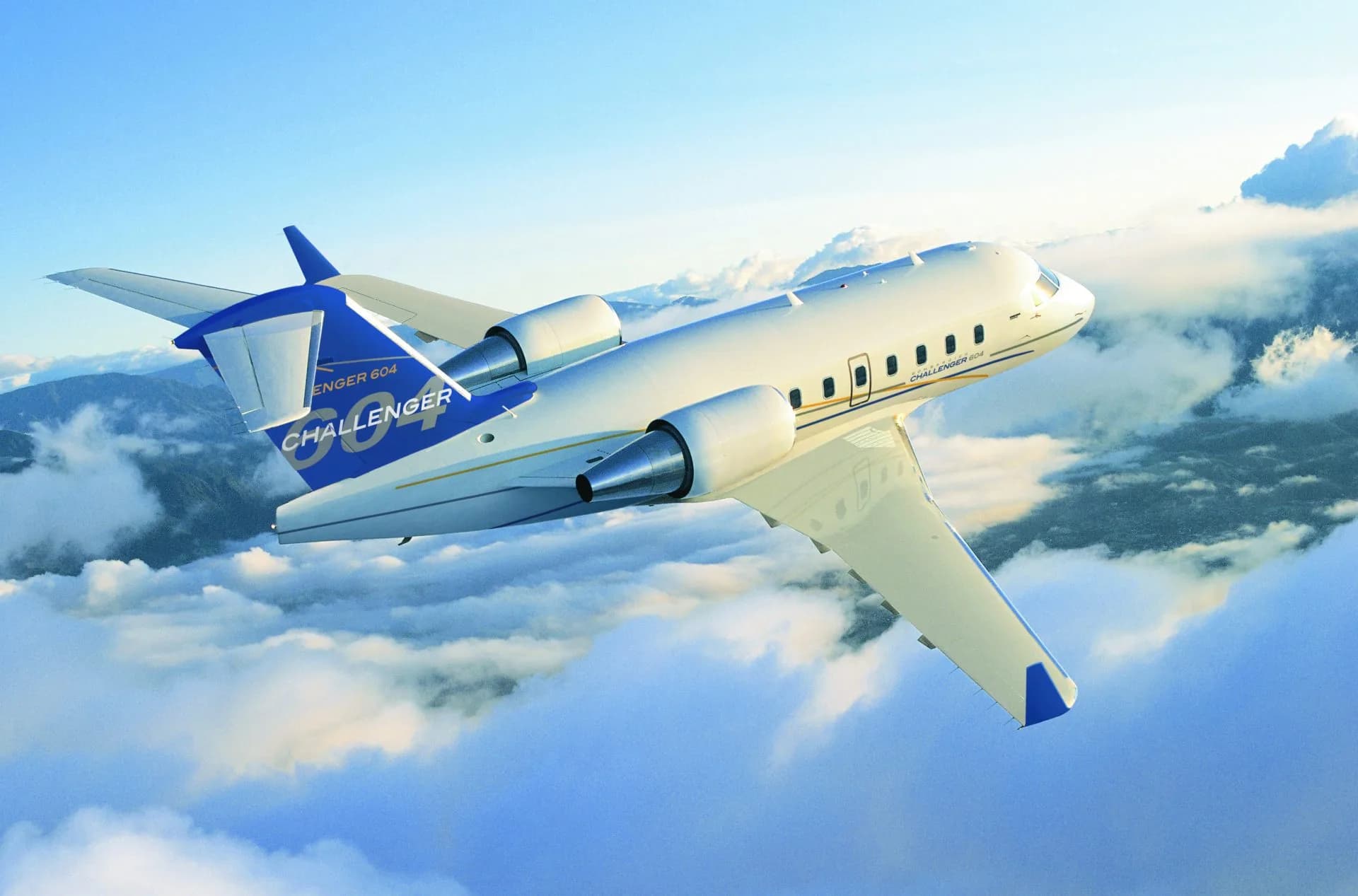 A white and blue Bombardier Challenger 604 business jet flies above clouds with mountains in the background.