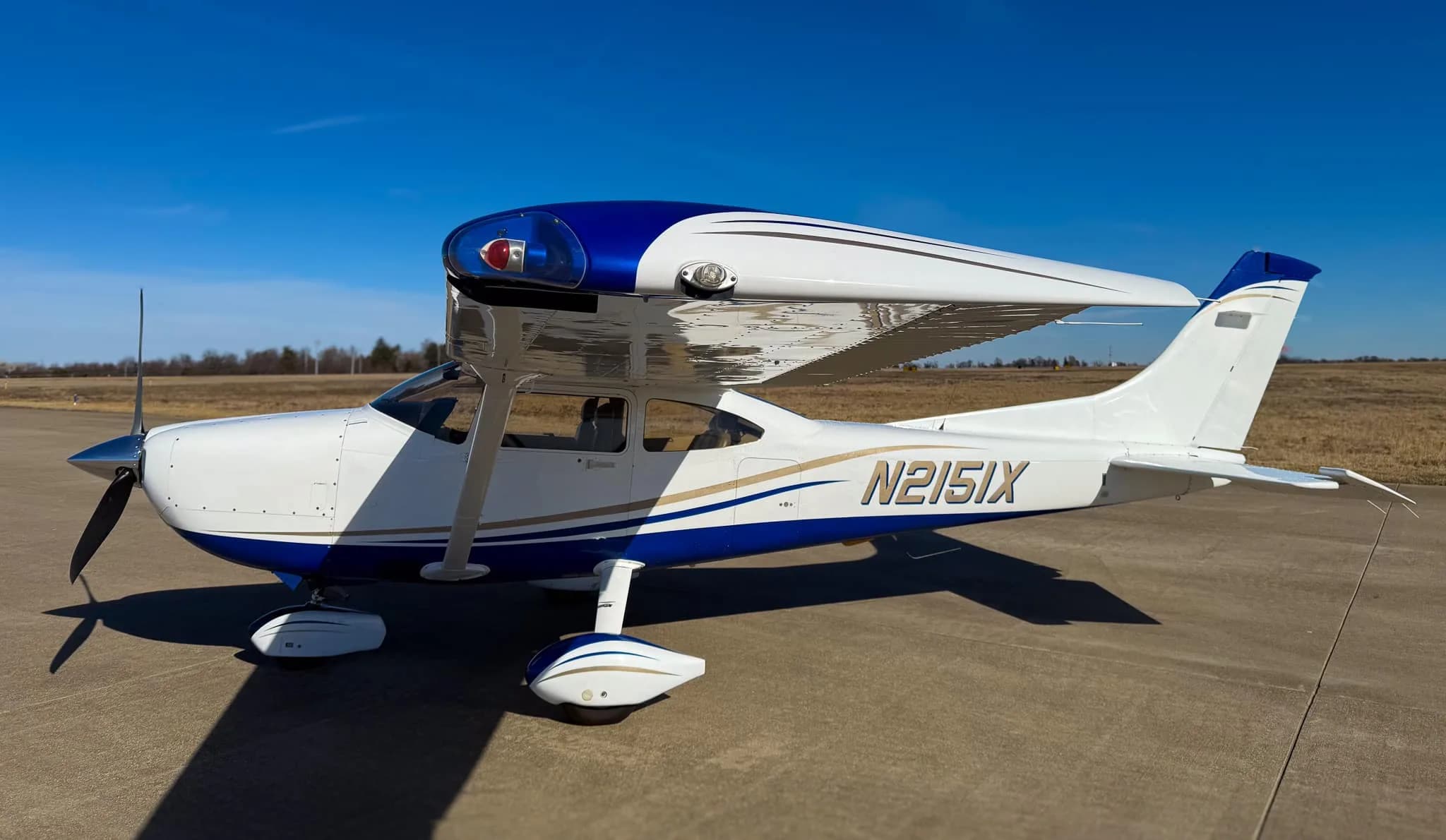 A close-up view of the right side of a white and blue Cessna 182 Skylane (N2151X) parked on a tarmac.