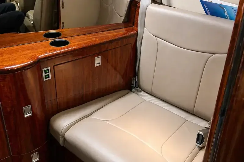 A single beige leather cabin seat is shown next to a wooden cabinet with cup holders and a mirrored surface.
