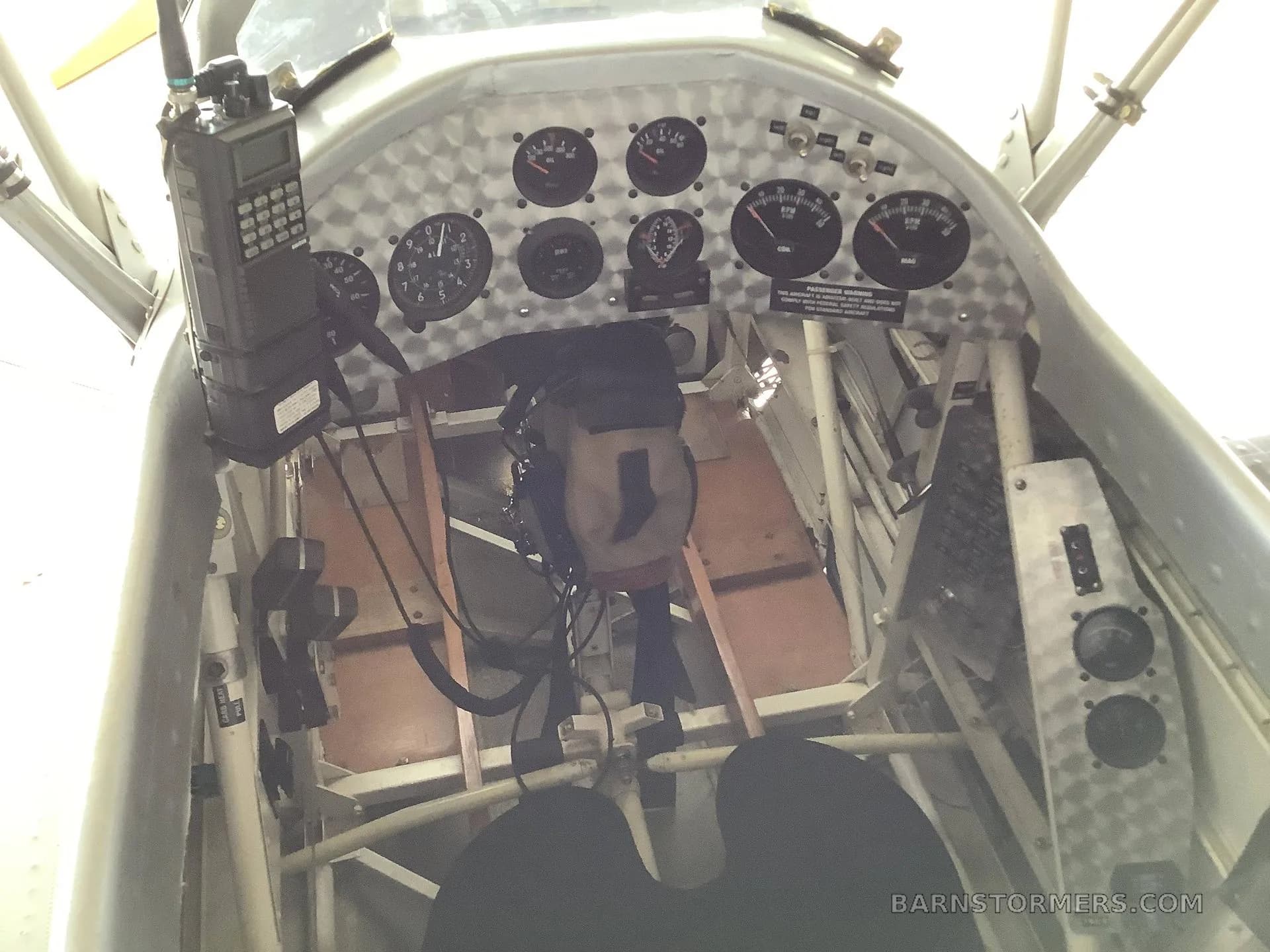 The cockpit of a biplane features a metal instrument panel with gauges and a handheld radio.