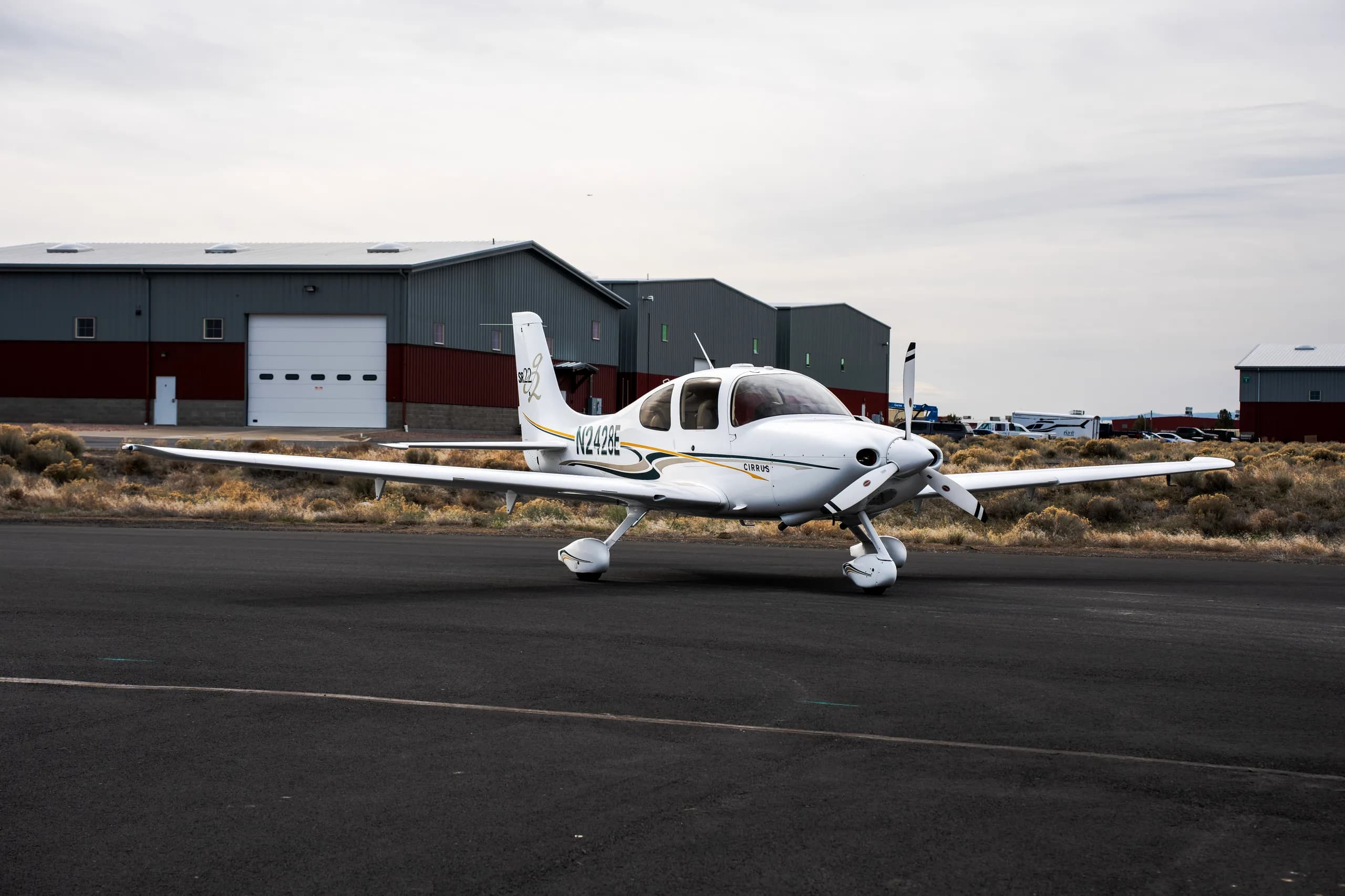 A white Cirrus SR22 aircraft with tail number N2147R, parked on an airfield in front of hangars.