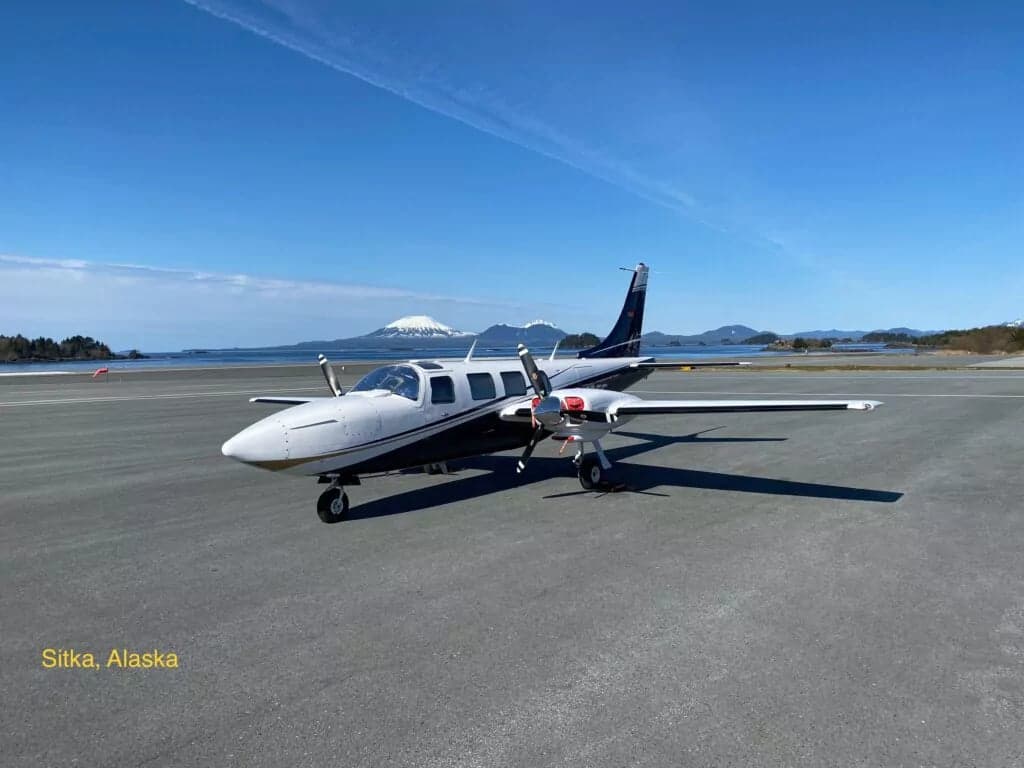 A Beechcraft Baron aircraft parked on a runway with a mountain and ocean in the background in Sitka, Alaska.