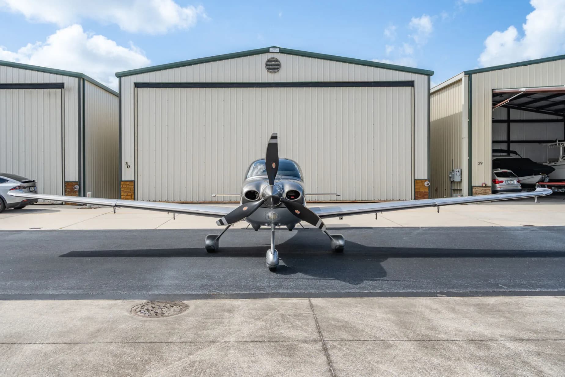 Front view of a silver Cirrus SR22T aircraft (N3404) parked on an airport tarmac in front of hangars.