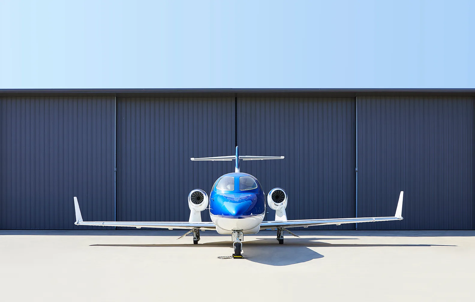 Front view of a blue and white HondaJet N856WD parked on an airfield in front of a hangar.