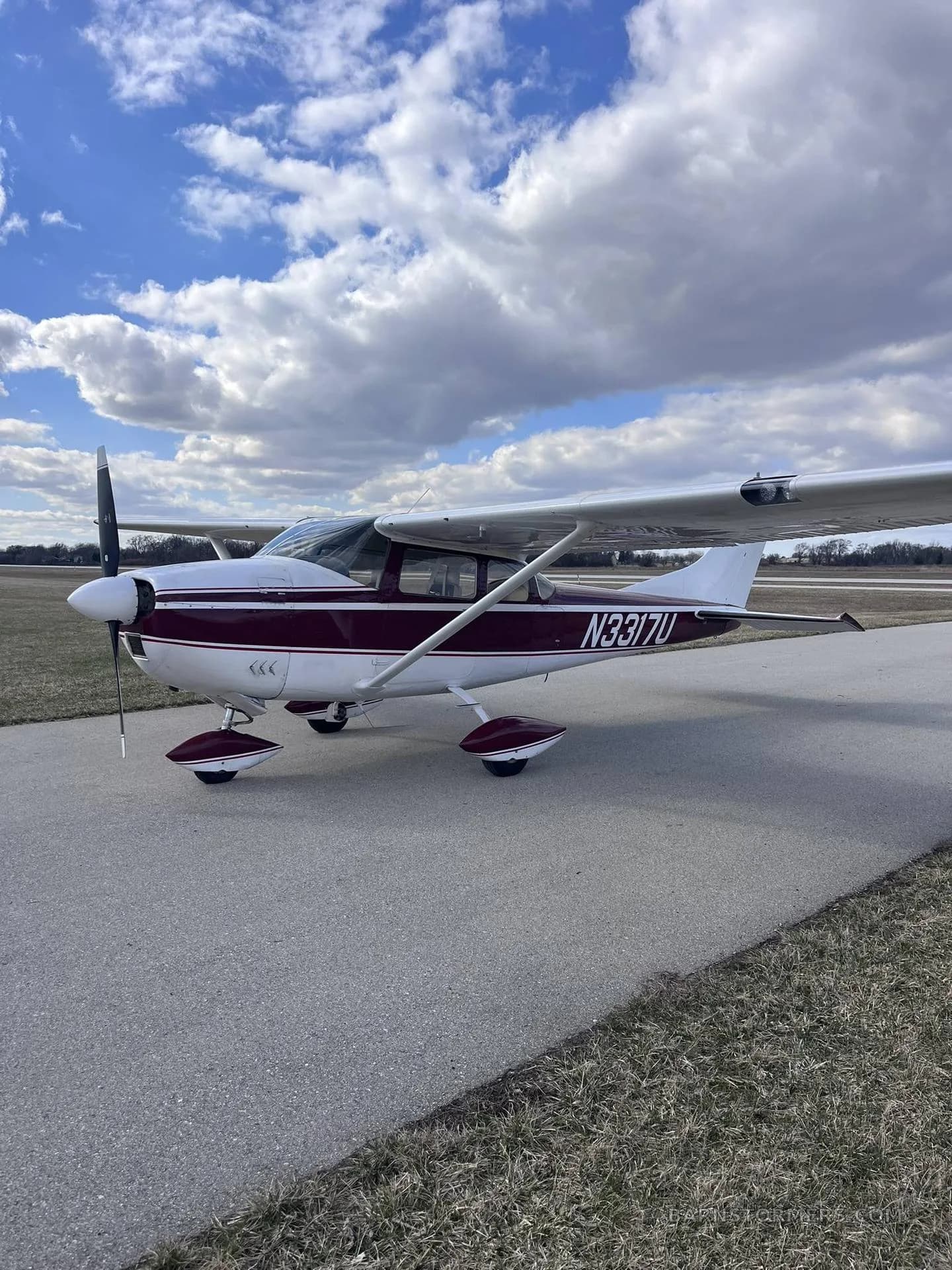 A maroon and white single-engine propeller aircraft (N3317U) parked on an asphalt taxiway under a partly cloudy sky.