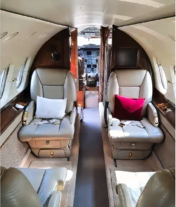 The interior cabin of a private jet with beige leather seats and a view towards the cockpit.