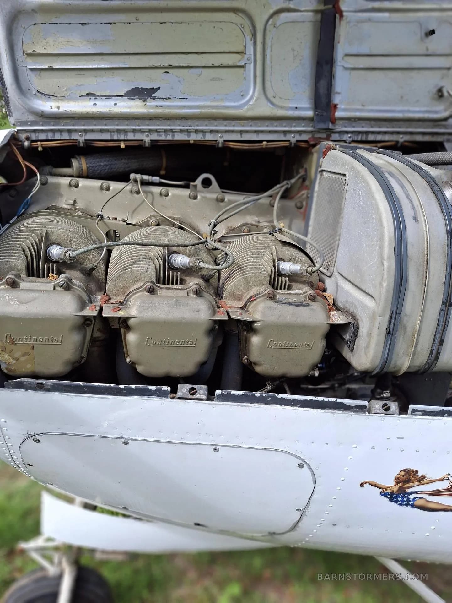 A close-up view of an aircraft's open engine cowling, revealing a Continental engine with three cylinders.
