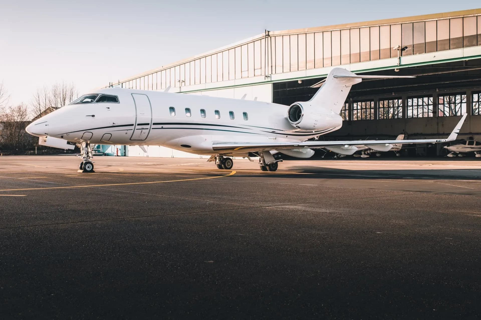 A white jet with black trim sits on the tarmac in front of a hangar.