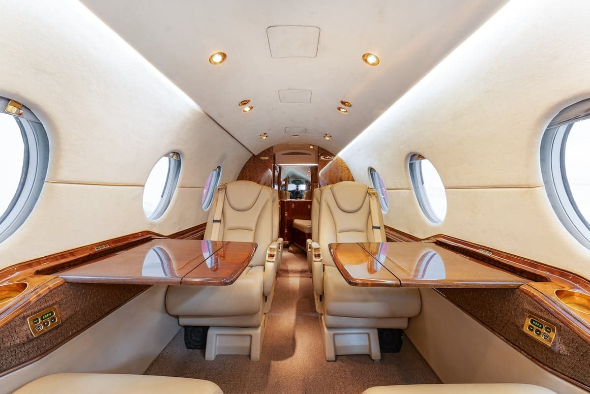 Aircraft interior with tan leather seats, wood trim, and fold-out tables.