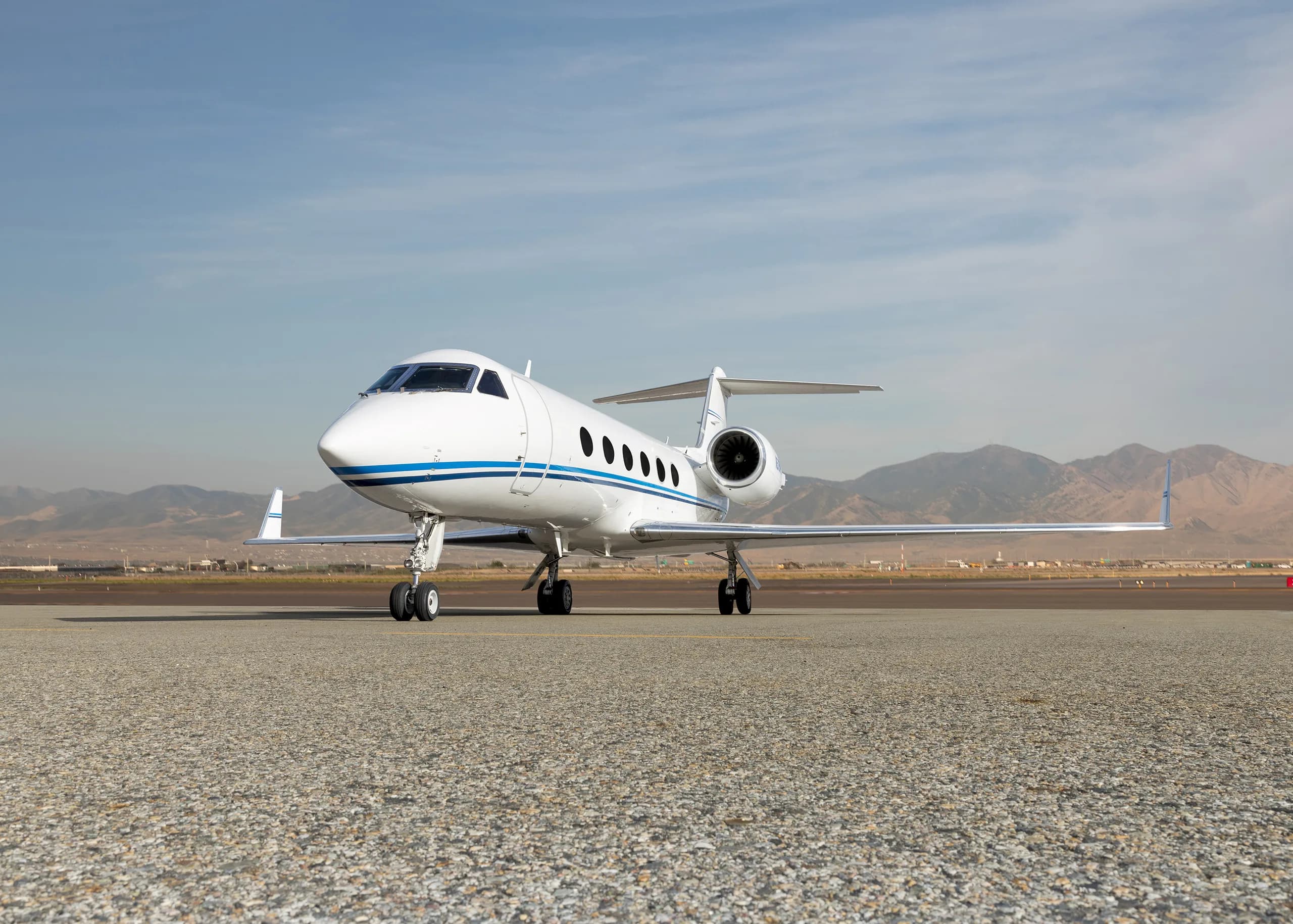 A white Gulfstream G550 business jet with a blue stripe parked on the tarmac, viewed from the front.