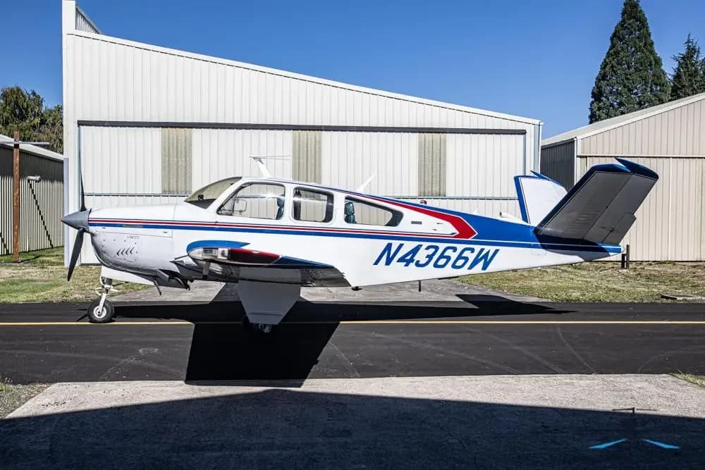 A Beechcraft Bonanza with registration N4366W is parked on the tarmac in front of a hangar.