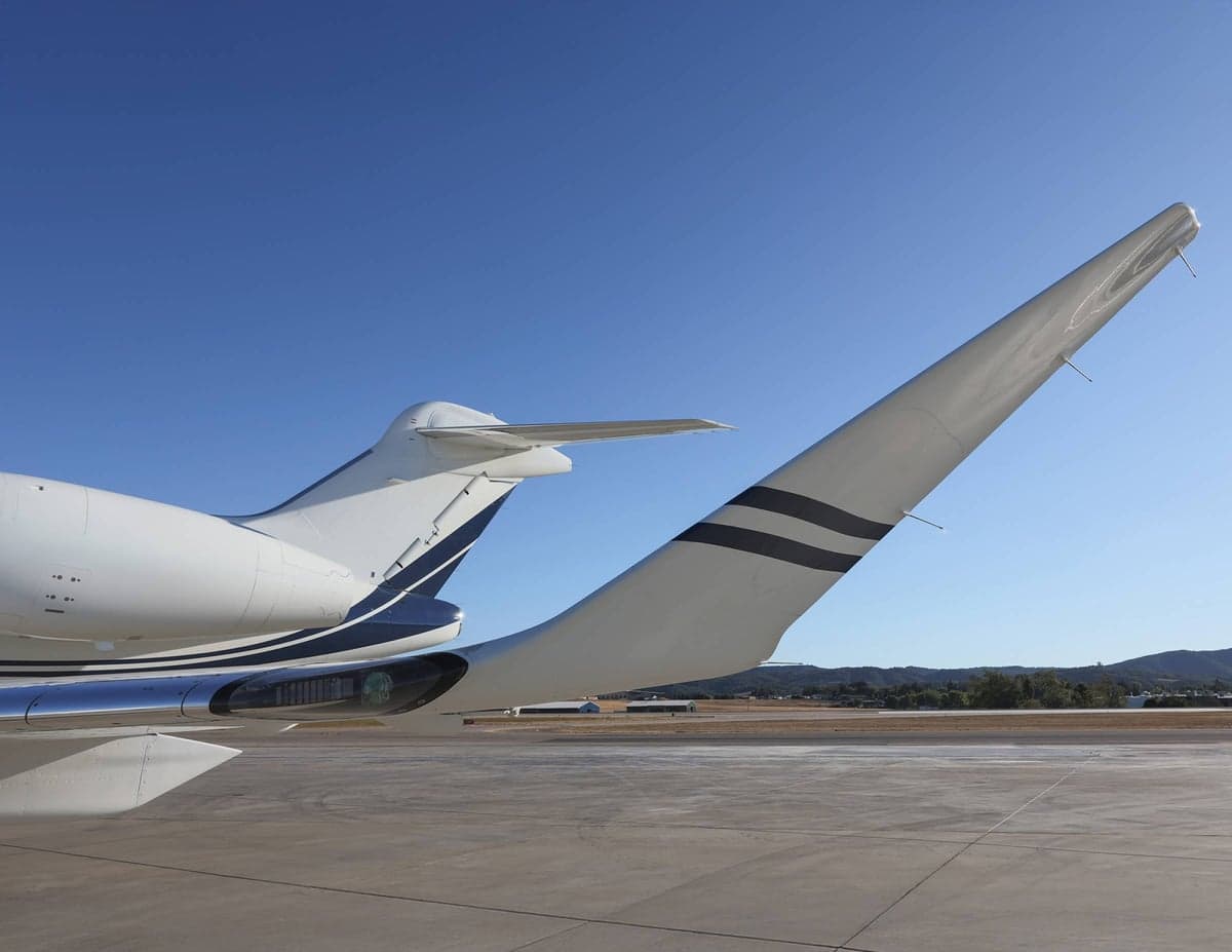 Close up of the tail and wing of a white aircraft with blue accents on the tarmac.