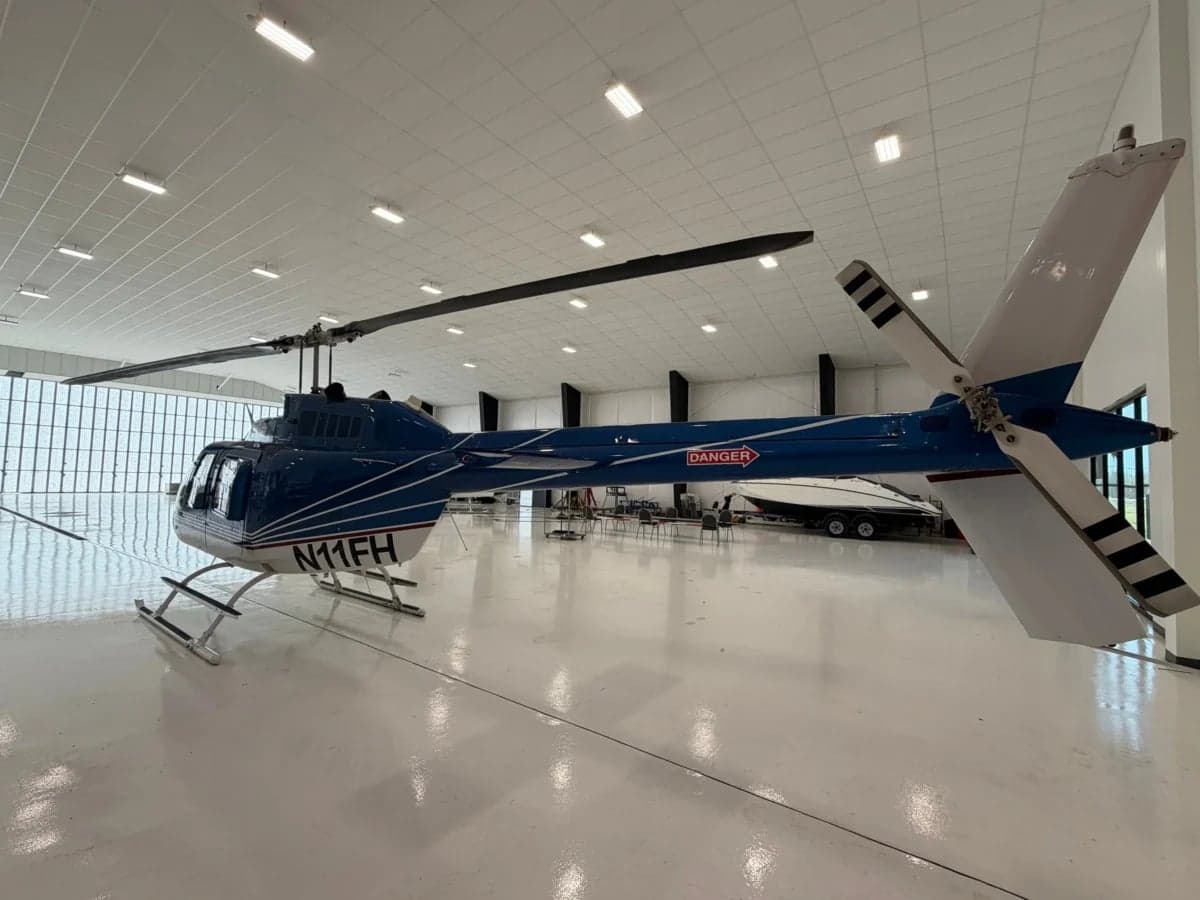 A blue and white Bell 206B JetRanger helicopter parked in a hangar, showing the tail number N11FH.