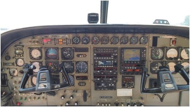 A detailed view of the aircraft's instrument panel, showing various gauges, avionics, and control yokes.