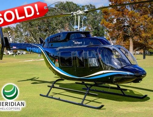 A black Bell 206L-4 helicopter with blue and white accents is parked on the grass.