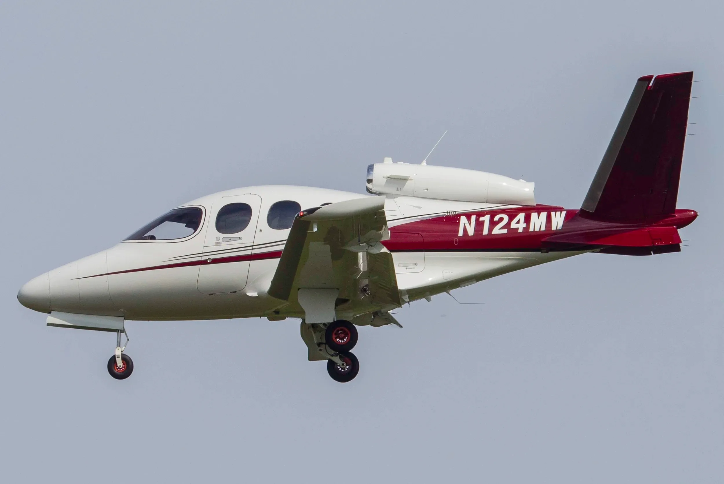 A Cirrus Vision Jet with registration N124MW is shown in flight with a white and maroon paint scheme.
