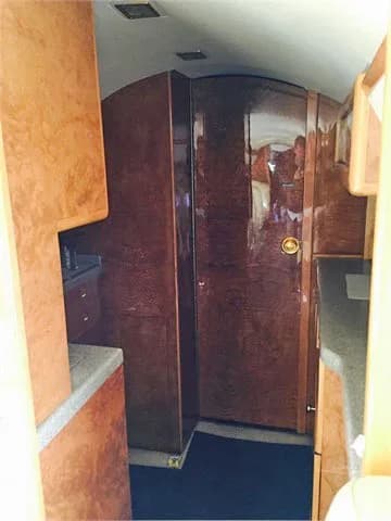 A view of the private jet's galley or lavatory area, featuring rich wood paneling and a closed door.