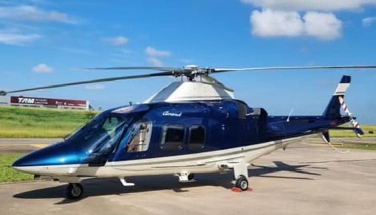 A blue and white AgustaWestland AW109 Grand helicopter is parked on the tarmac.