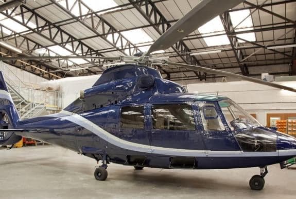 A dark blue helicopter sits in a hangar.