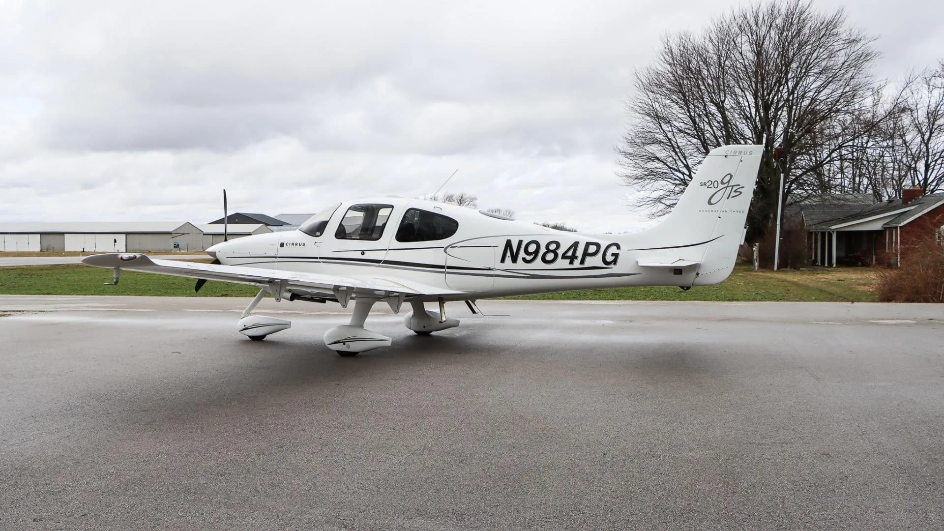 A white Cirrus SR20 GTS aircraft, N984PG, is parked with its right side visible on a wet tarmac.