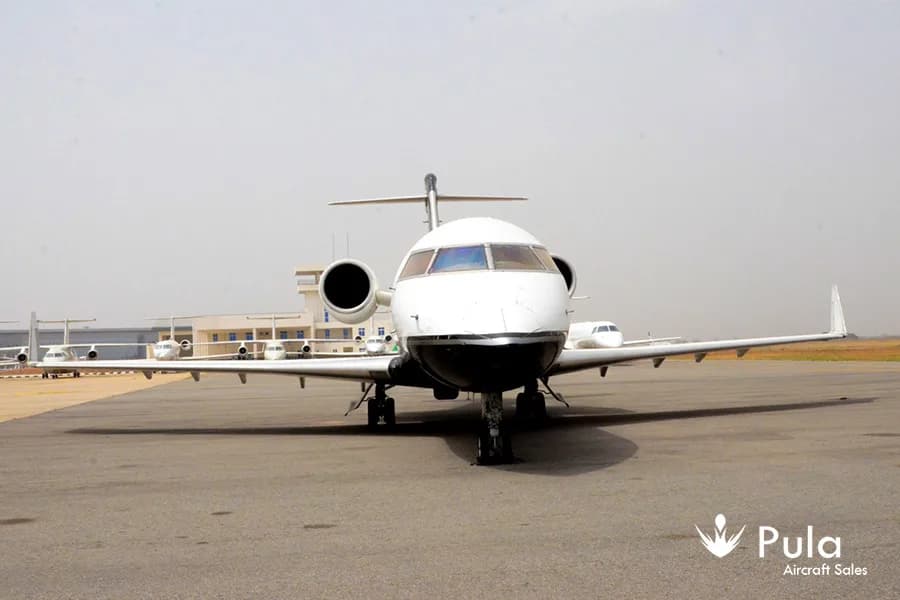 A front view of a white and black Bombardier Challenger 604 business jet (N64JS) on a tarmac.