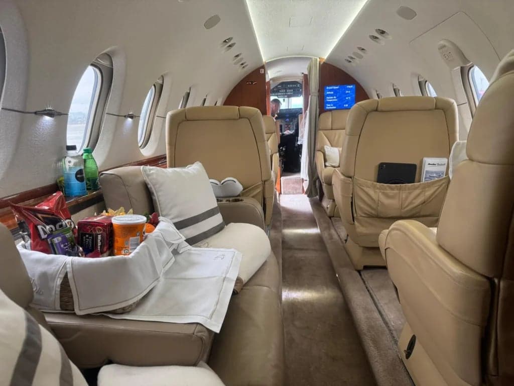 A view of the aircraft's interior with tan leather seats, pillows, and a tray with snacks and drinks.