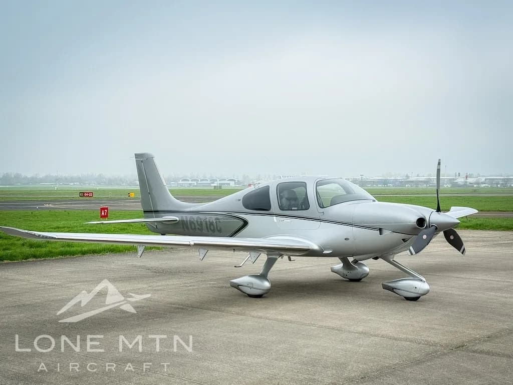 A silver Cirrus SR22 aircraft, registration N6918C, parked on an airfield with runway markings visible.