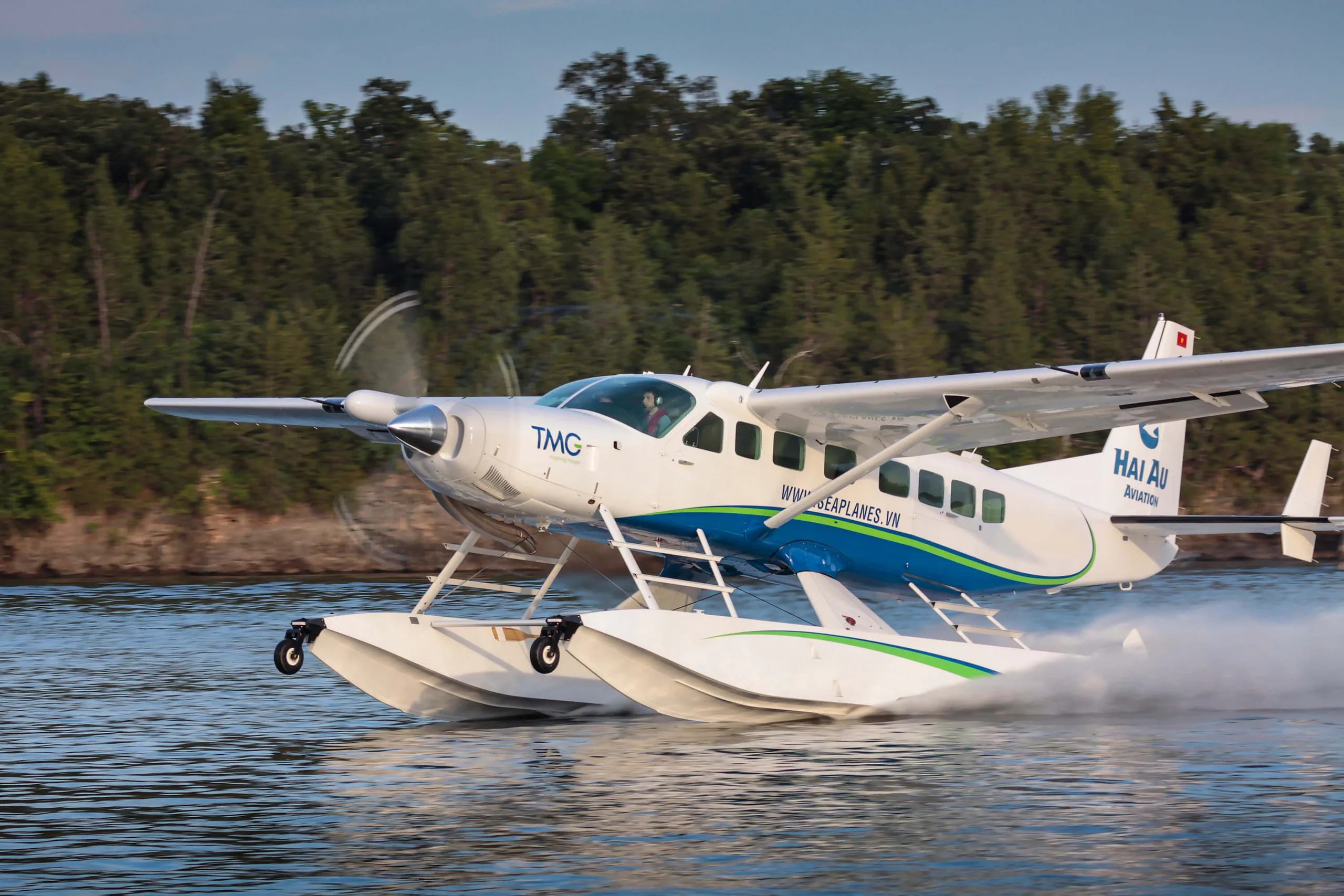 A white and blue seaplane with the logo 'HAI AU Aviation' is shown on the water.