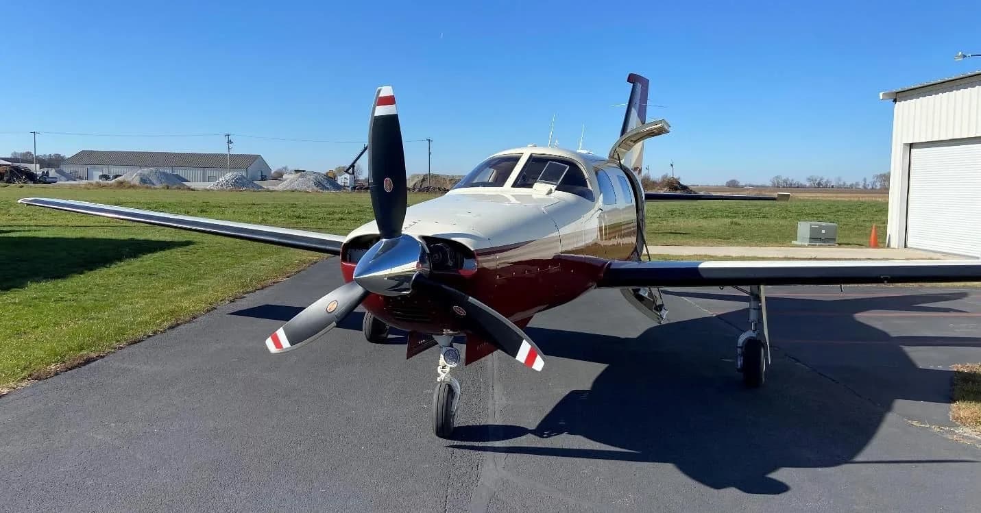 Front view of a Piper Malibu Mirage (N13PC) with a three-bladed propeller, parked on an asphalt ramp.