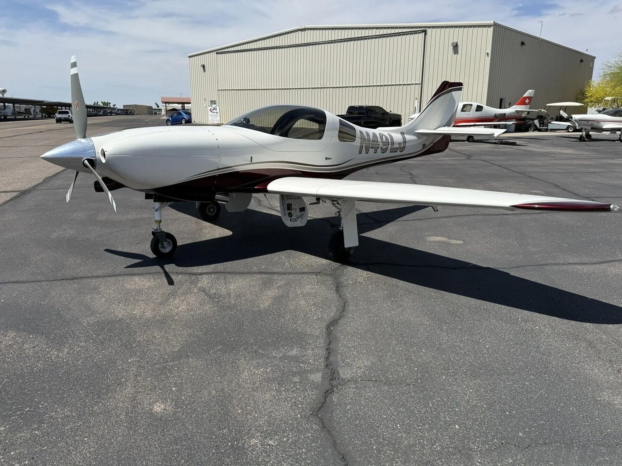 A white and maroon single-engine aircraft (N49LJ) parked on an asphalt apron with other aircraft in the background.