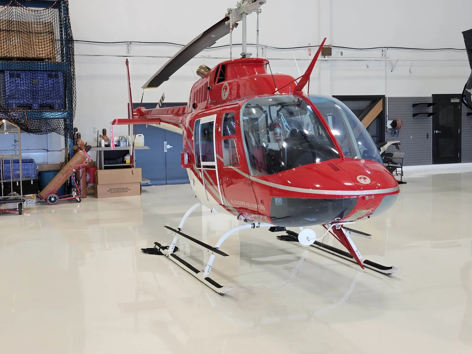 A red and white helicopter with skis on its landing gear is parked inside a brightly lit hangar.