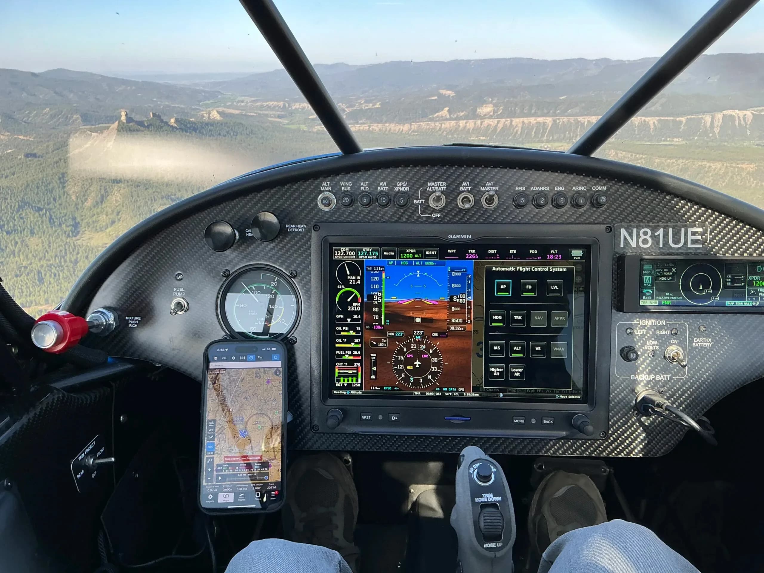 The cockpit view during flight, showing the instrument panel with a Garmin G3X Touch display and a scenic mountainous landscape outside.