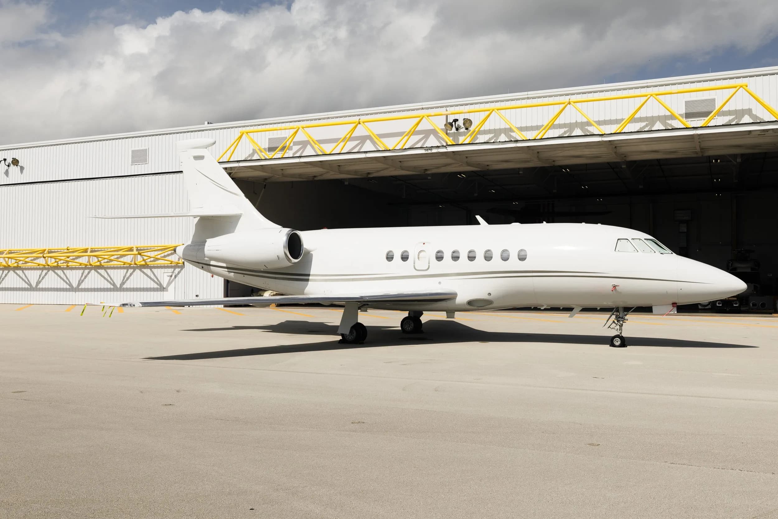 A white Dassault Falcon business jet parked outside a hangar with yellow structural beams.