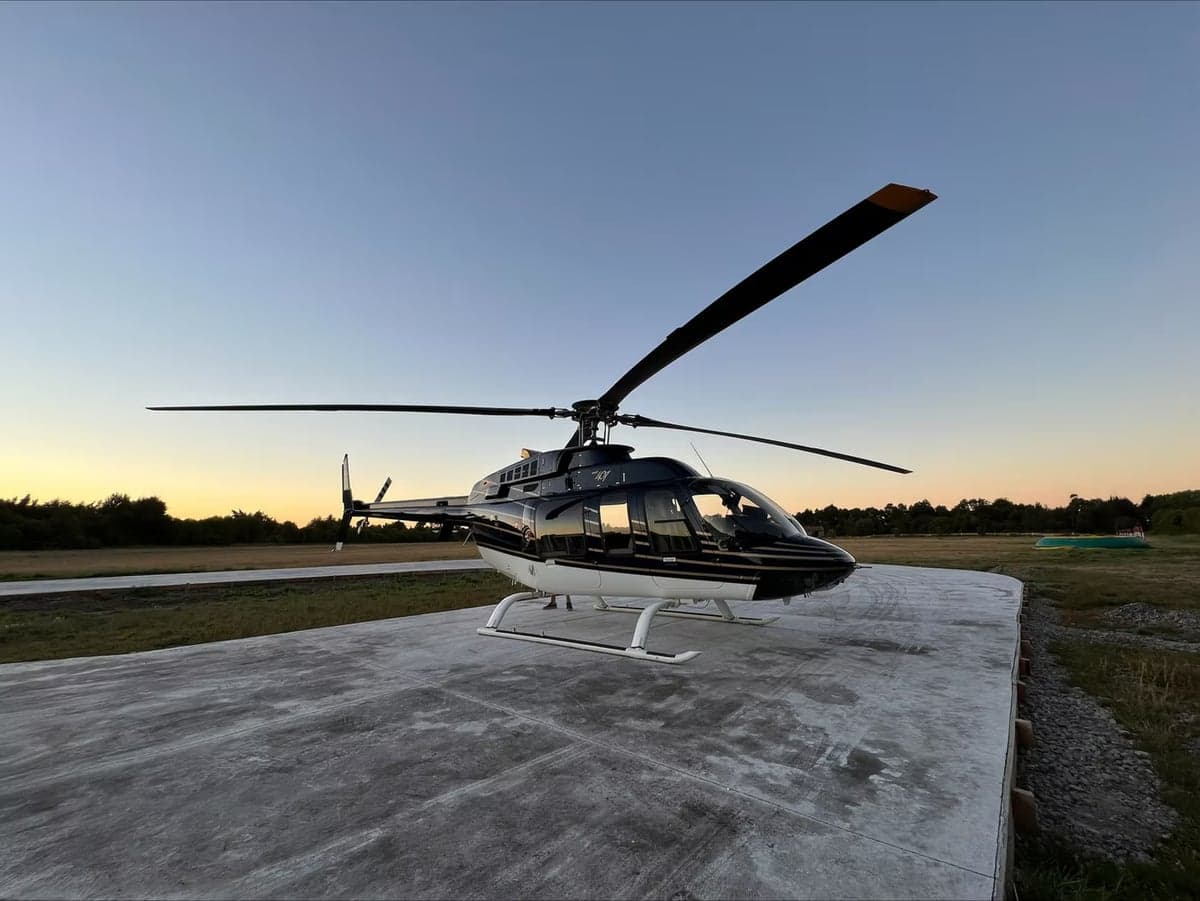 A Bell 407 helicopter in a black and white paint scheme is shown on a helipad at dusk.