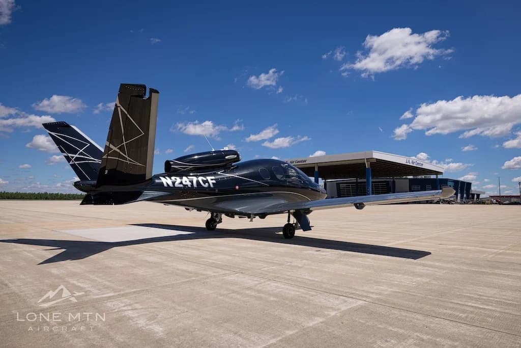 A black Cirrus Vision Jet (N247CF) with a unique tail design parked on an airport tarmac in front of an FBO building.
