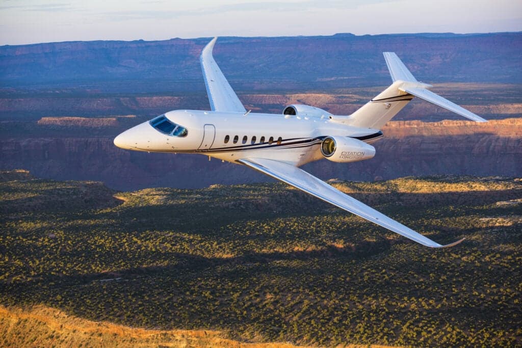 A Citation Longitude jet in flight over a canyon landscape.