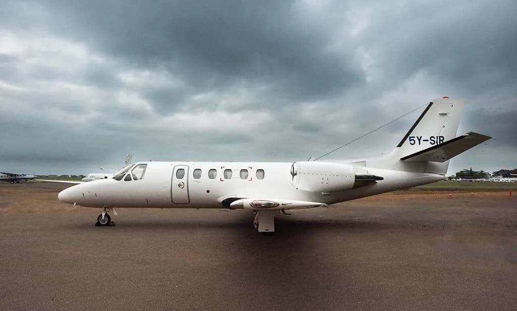 A white Cessna Citation business jet with registration 5Y-SIR parked on an airport tarmac under a cloudy sky.