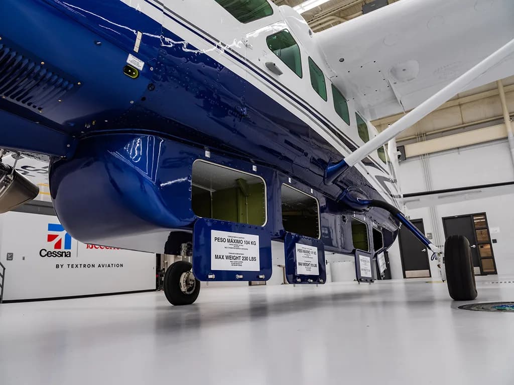 A close-up of the blue underside cargo pods of the Cessna Caravan with their doors open, showing weight limits.