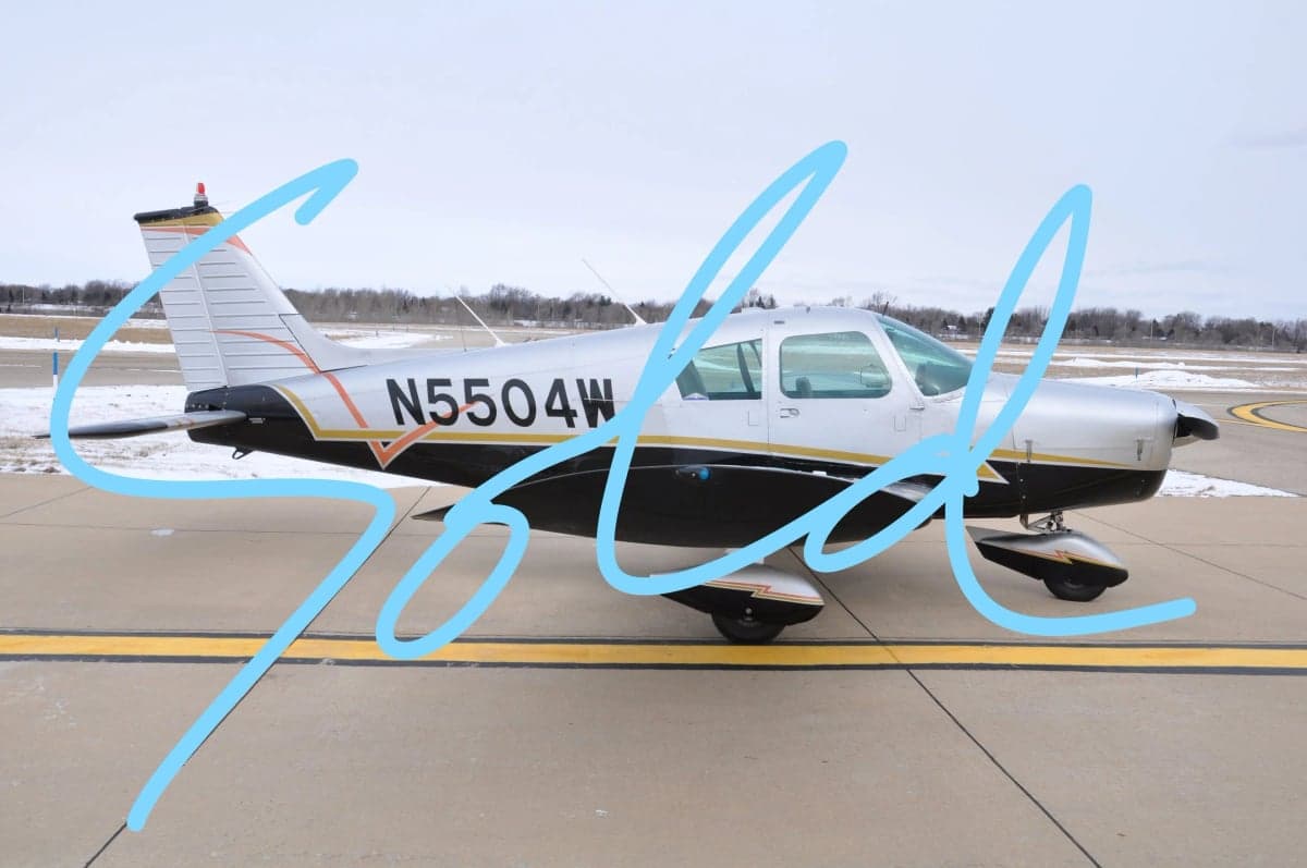 Side view of a Cessna 182 Skylane with a silver, black, and gold paint scheme on the tarmac.