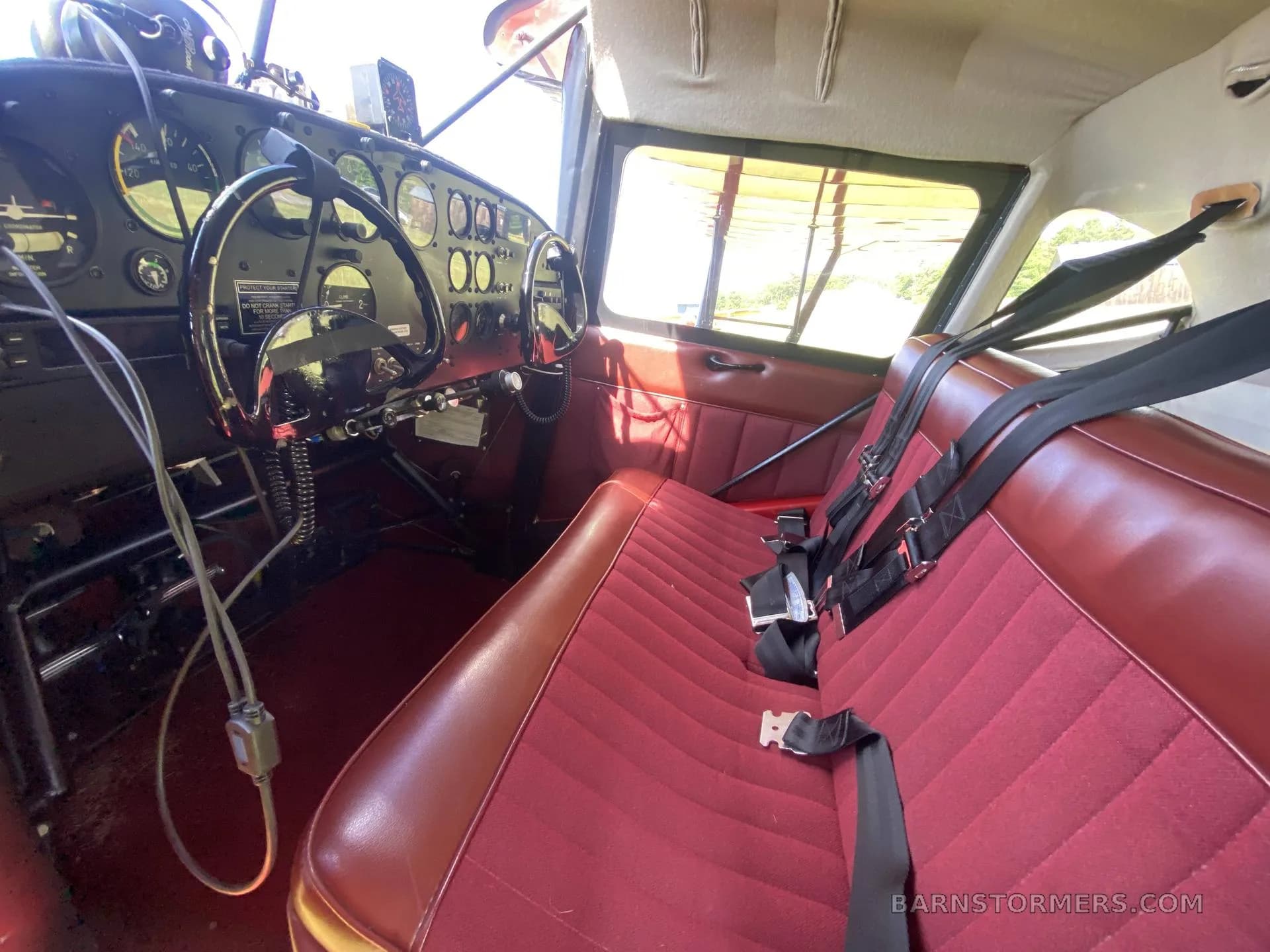 The interior of a small aircraft with red upholstered seats and a visible instrument panel.