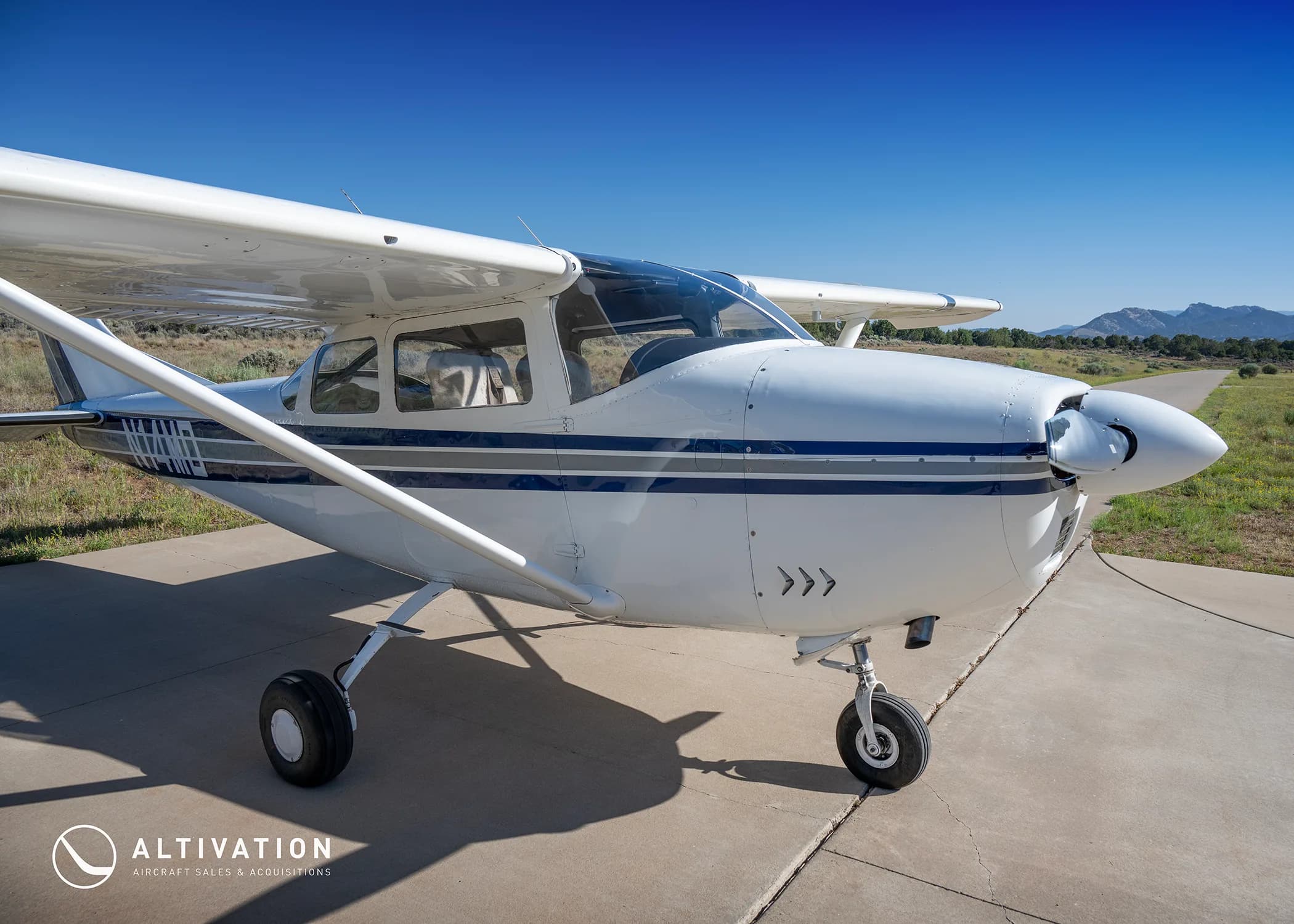 A close-up front-right view of a white Cessna 182 with blue and grey stripes, registration N74MD, on a concrete apron.